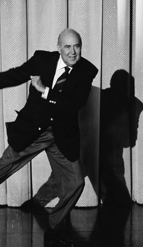 Black and white wallpaper of Carl Reiner in playful pose with dramatic lighting and textured curtain