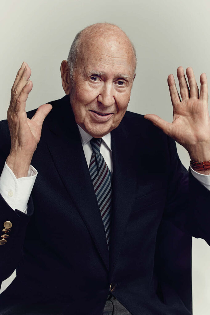 Carl Reiner in sharp suit and striped tie smiling warmly on light background wallpaper