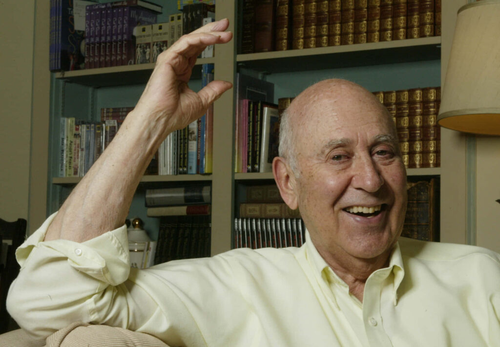 Carl Reiner smiling warmly in cozy room with bookshelves of classic literature and soft lighting Wallpaper