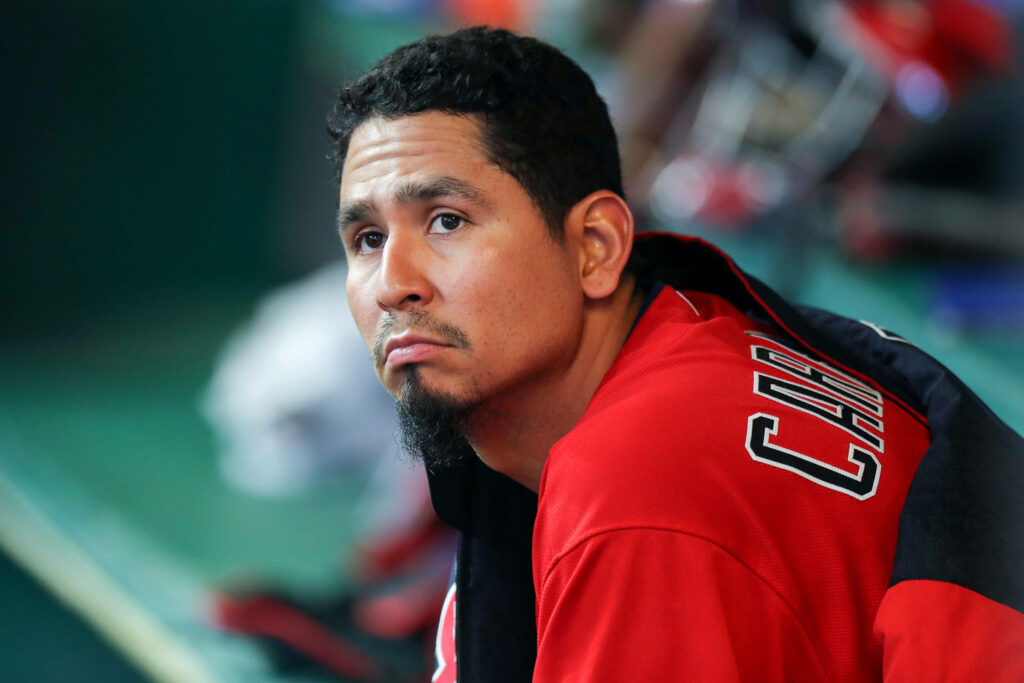 Cleveland pitcher Carlos Carrasco in red and black uniform sitting in dugout thoughtful pose Wallpaper