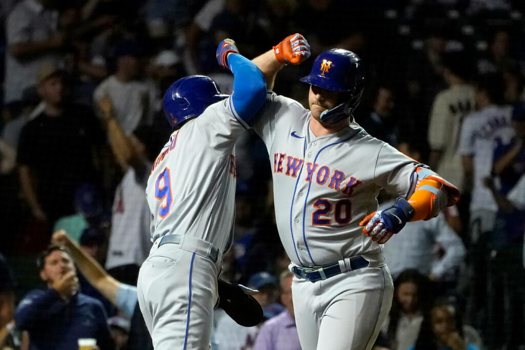 Carlos Carrasco and Mets teammate bump elbows in energetic night baseball game with vibrant uniforms Wallpaper