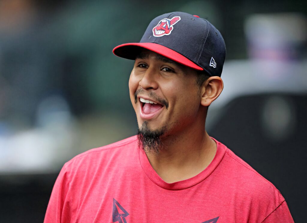 Carlos Carrasco smiling warmly in pink shirt and Cleveland baseball cap with soft natural light Wallpaper