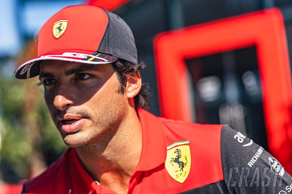 Carlos Sainz Jr in Ferrari cap and uniform with vibrant sunlit Formula 1 racing backdrop wallpaper