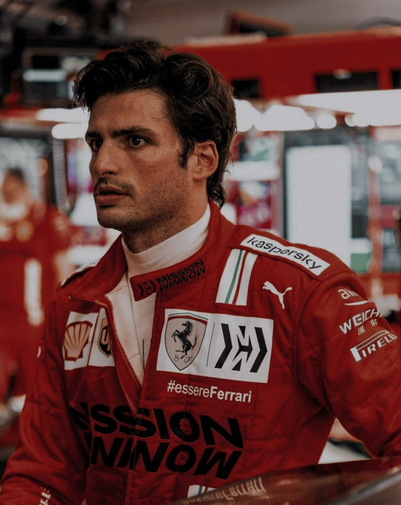 Carlos Sainz Jr in Ferrari racing suit side profile with vibrant red Formula 1 motorsport backdrop Wallpaper