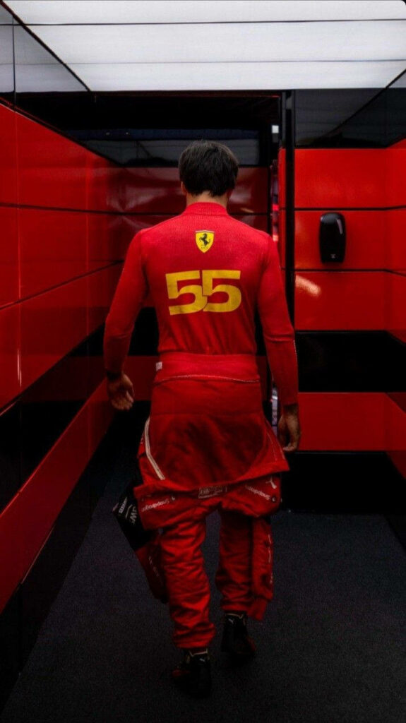 Carlos Sainz Jr in red Ferrari suit with number 55 walking through glossy red black corridor Wallpaper