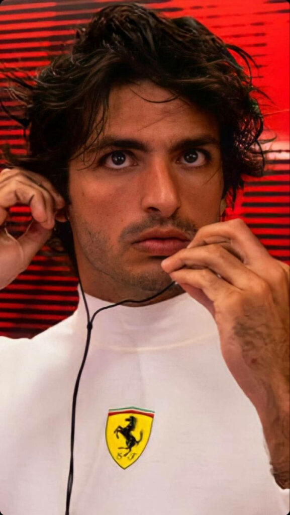 Carlos Sainz Jr focused in white Ferrari racing suit with earphones against vibrant red background Wallpaper