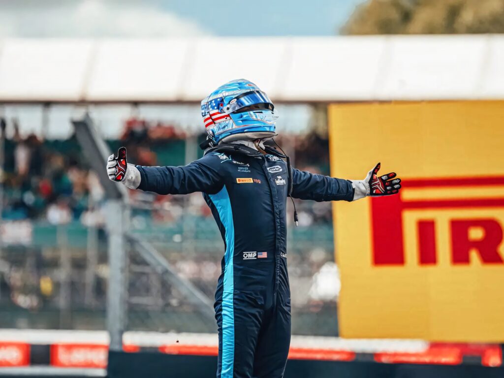Carlos Sainz Jr. celebrating victory on racetrack wearing blue and white racing suit and helmet Wallpaper