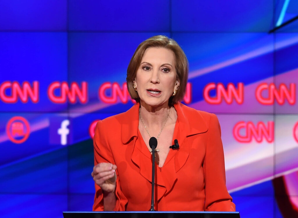 Carly Fiorina in vibrant red suit at CNN debate podium with illuminated logo and digital screens Wallpaper