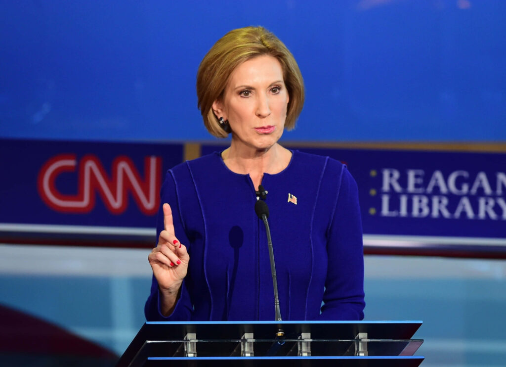 Carly Fiorina speaking at debate podium with CNN Reagan Library logos wearing blue suit and flag pin Wallpaper