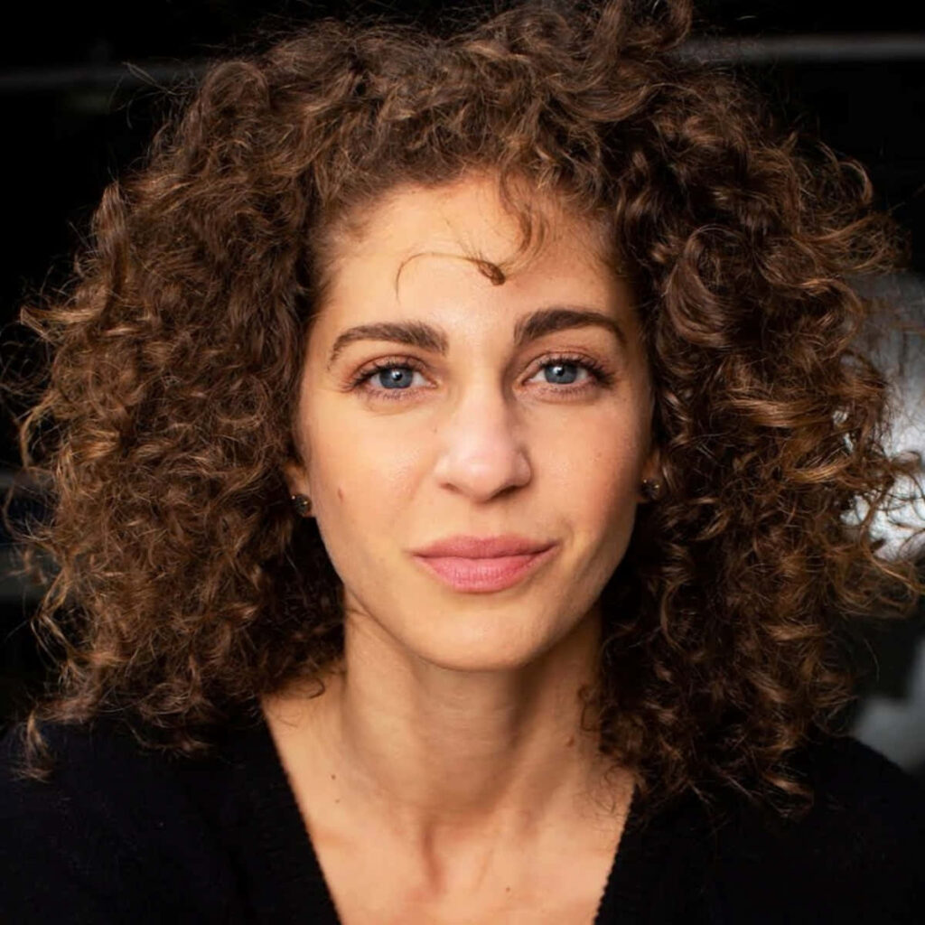 Carmel Amit portrait with curly hair soft makeup confident expression dark blurred background Wallpaper