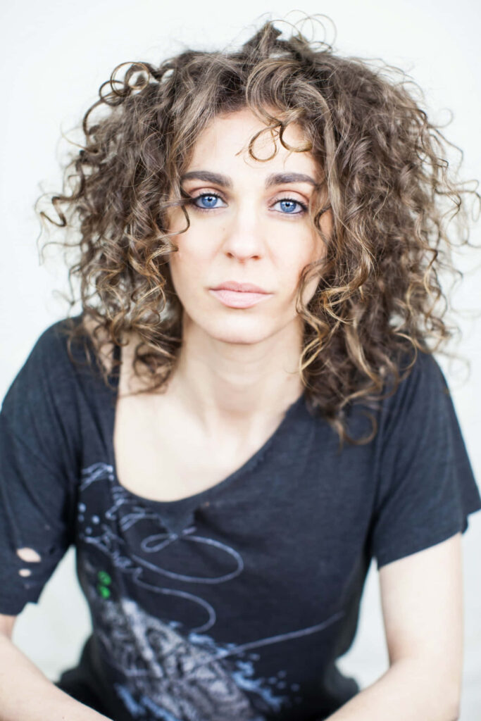 Carmel Amit portrait with curly hair and piercing blue eyes on soft light background wallpaper
