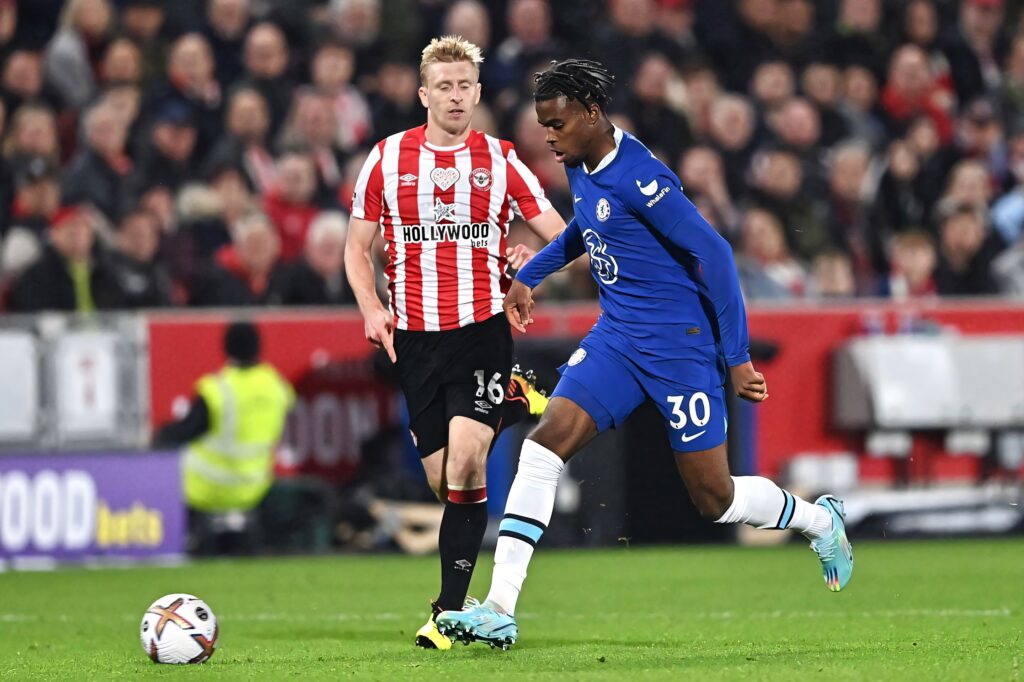 Carney Chukwuemeka in blue Chelsea kit chasing ball on green pitch during Premier League match Wallpaper