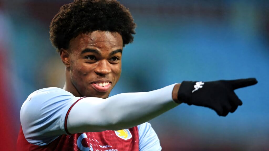 Carney Chukwuemeka smiling and pointing in team kit with black gloves on blue blurred background Wallpaper