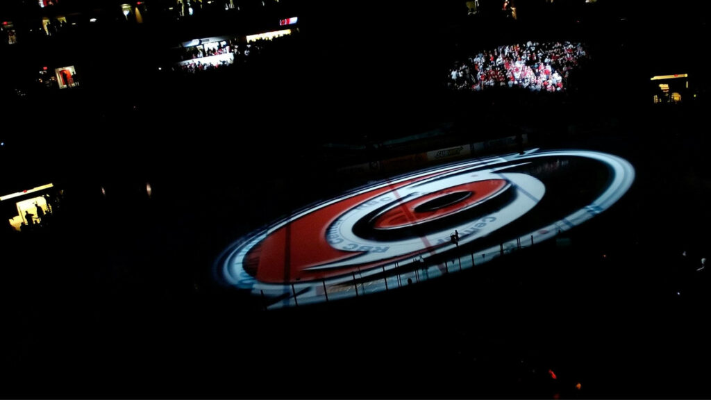 Carolina Hurricanes logo lit at center ice rink with vibrant crowd in dark arena wallpaper background