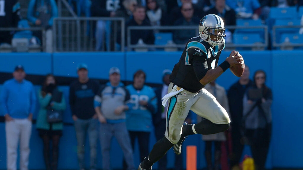 Carolina Panthers player mid-run in black blue uniform on vibrant football field with fans Wallpaper