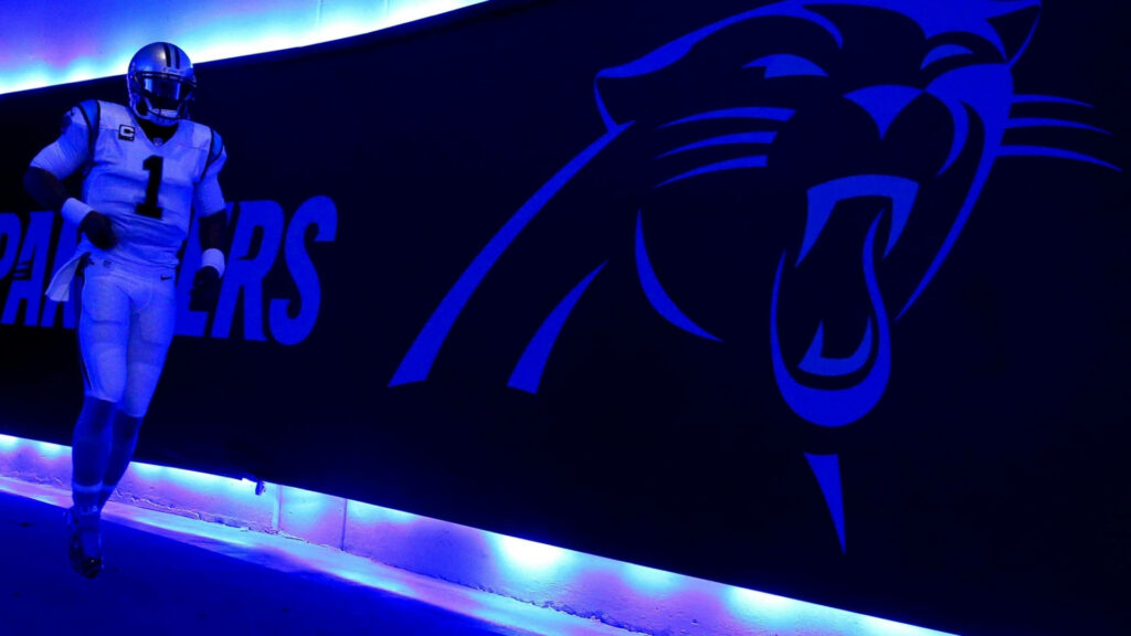 Carolina Panthers player by illuminated team banner with roaring panther logo and blue lights background Wallpaper