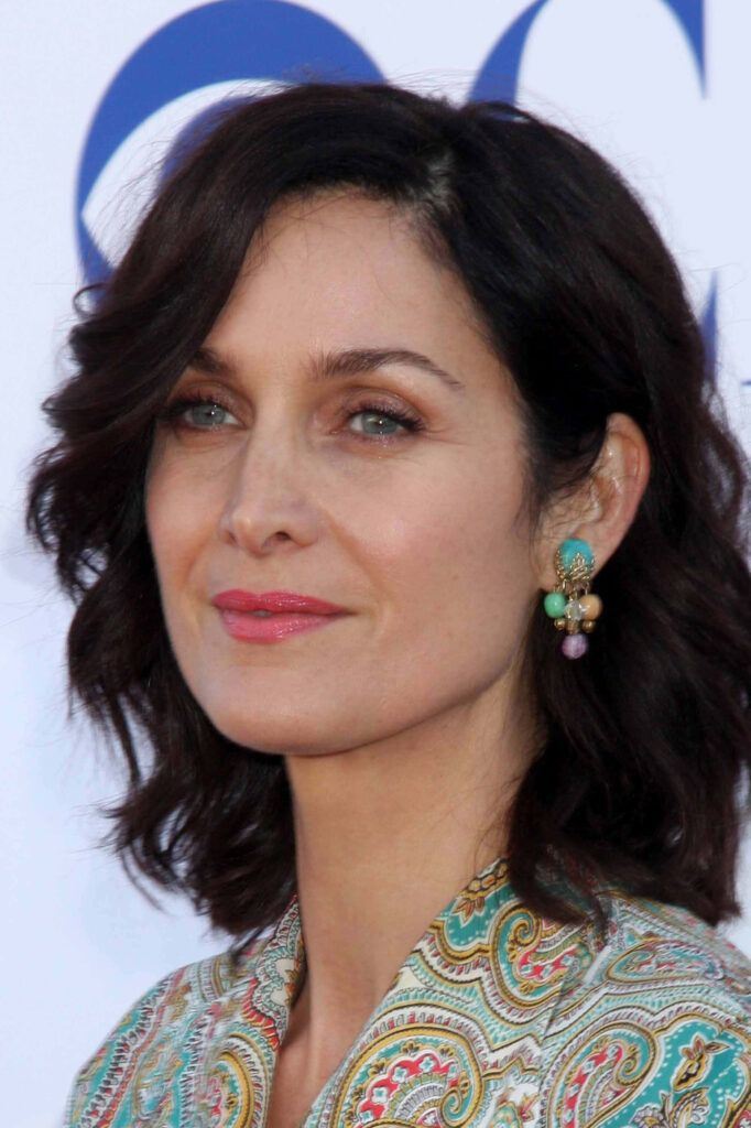Carrie-Anne Moss close-up portrait elegant dark hair vibrant patterned outfit intricate earrings Wallpaper
