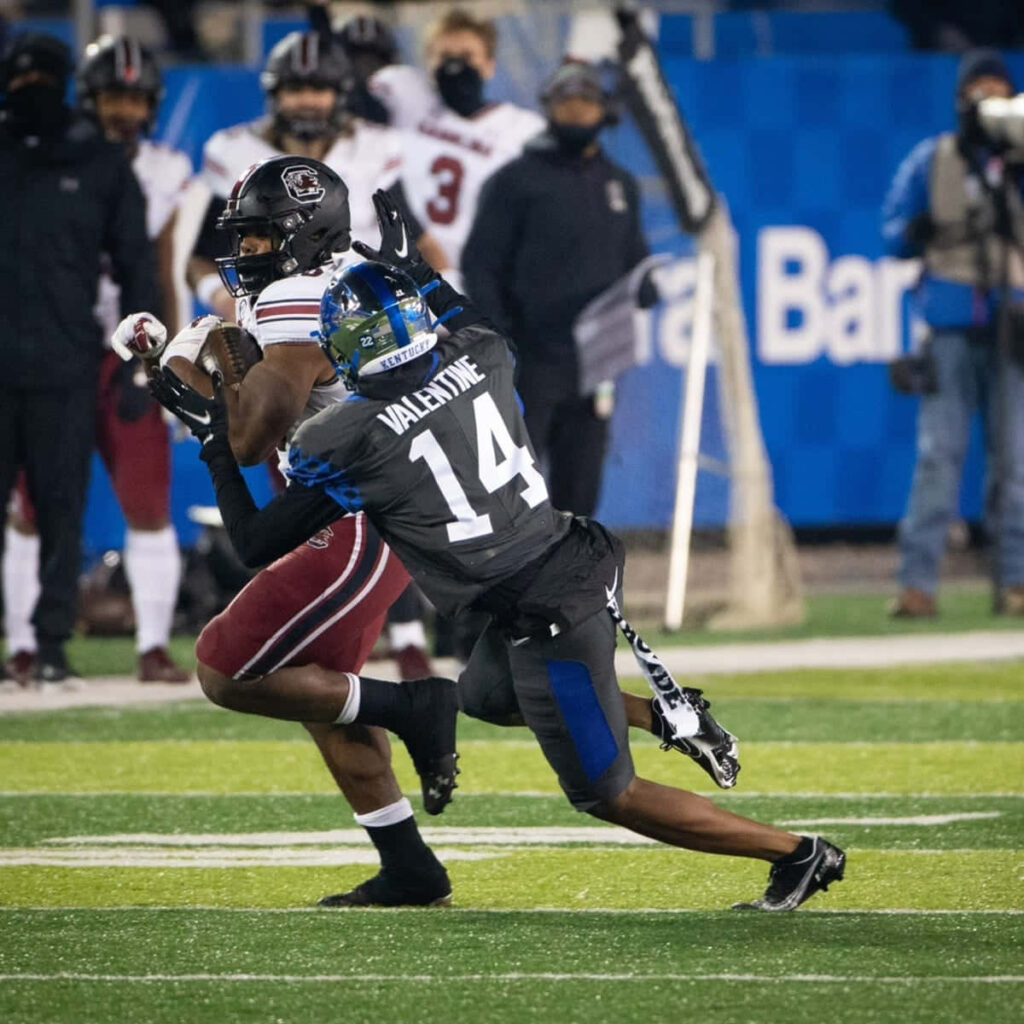Carrington Valentine in black jersey number 14 tackles opponent on vibrant football field at night Wallpaper