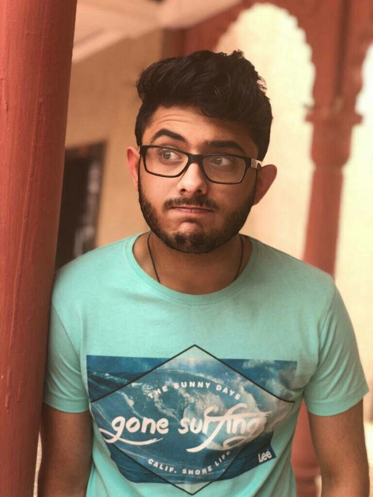 CarryMinati peeks behind red pillar in mint green shirt warm blurred background wallpaper
