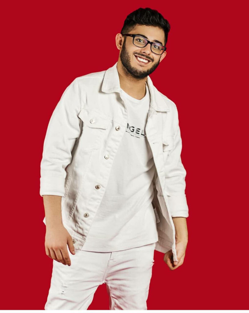 CarryMinati confident in white jacket and jeans against red background modern casual style wallpaper