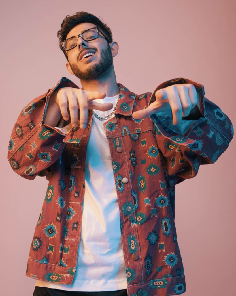 CarryMinati iPhone wallpaper with rust-red jacket playful pose soft pink background vibrant energy