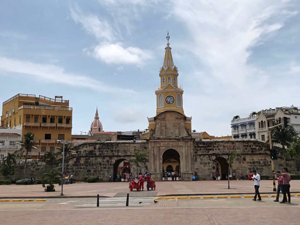 Front view of Cartagena Yellow Clock Tower with colonial buildings and vibrant city square background Wallpaper