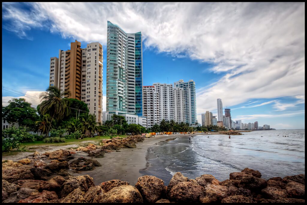 Rocky beach in Cartagena Colombia with high-rise buildings coastal skyline under blue sky Wallpaper