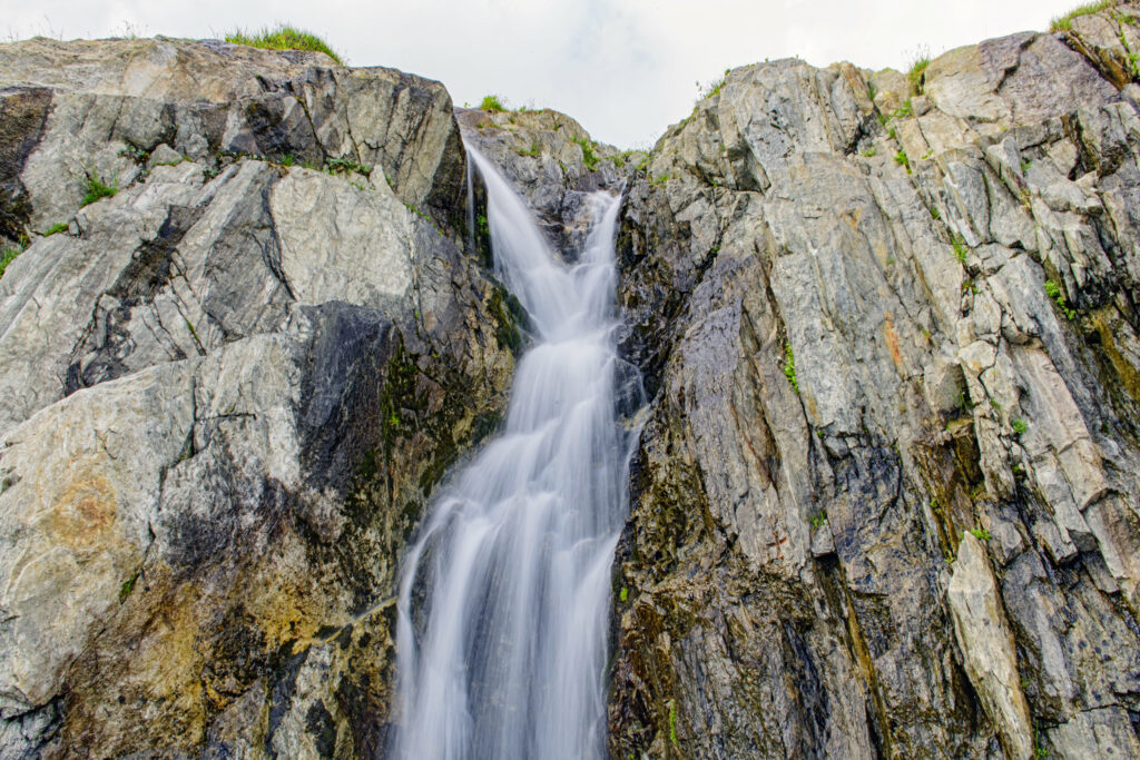 Cascading waterfall over rugged rocks with bright sky natural scenic outdoor wallpaper background
