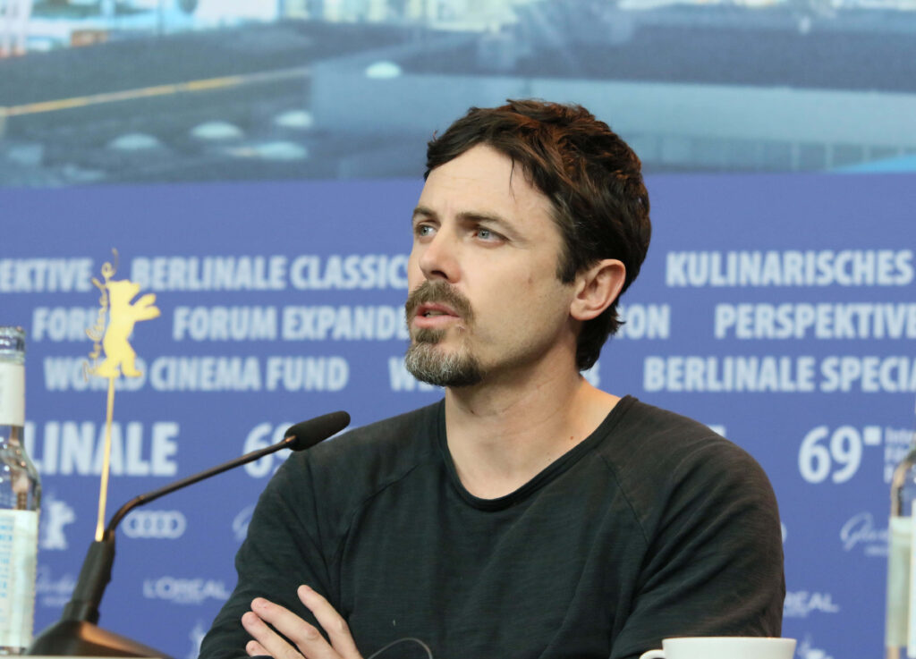 Casey Affleck casual style at press event blue background white text cinematic wallpaper