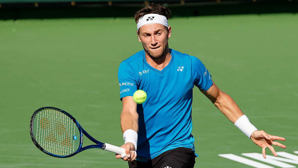 Casper Ruud focused mid-match on green tennis court returning fast ball showcasing athletic skill Wallpaper