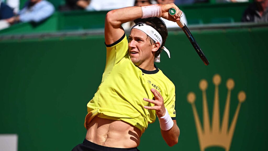Casper Ruud mid-swing in vibrant yellow shirt on green tennis court showing focus and motion Wallpaper