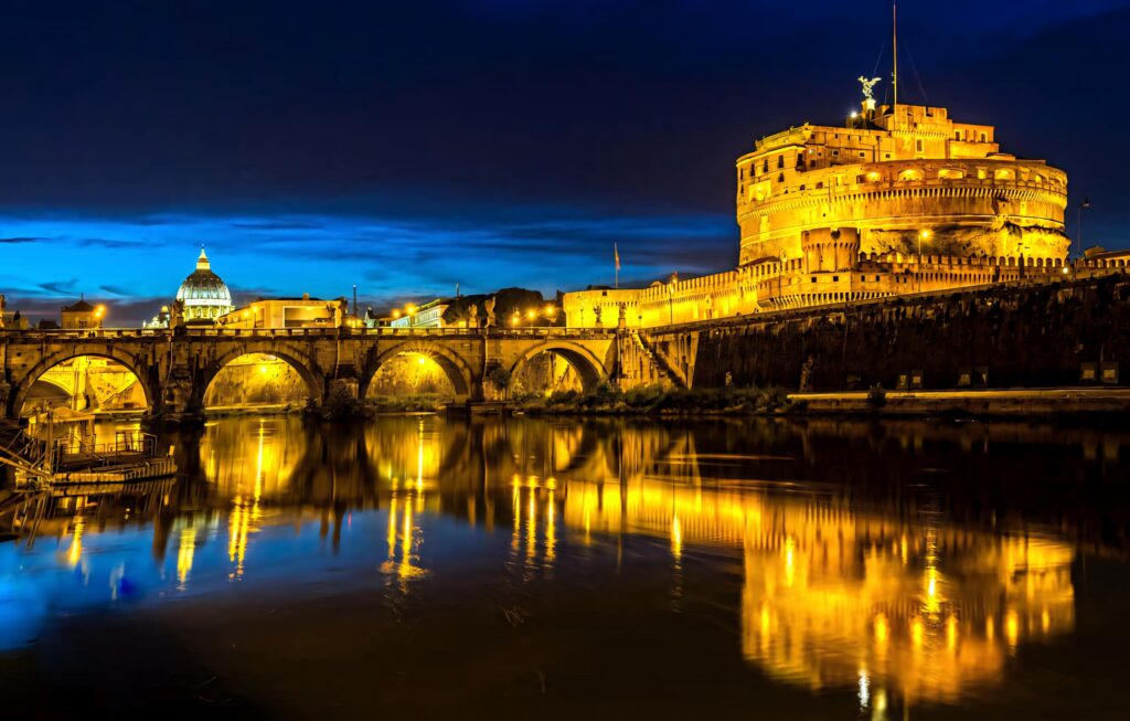 Castel Sant Angelo illuminated at night with golden lights reflecting on calm river below Wallpaper