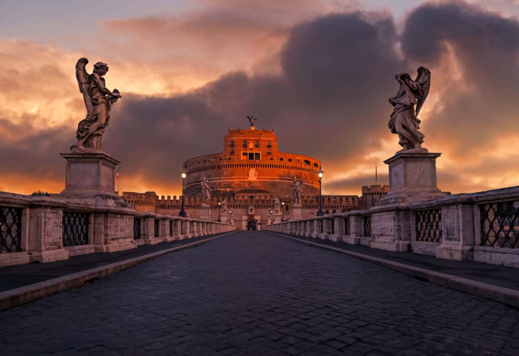 Castel Sant Angelo at sunset with angel statues on stone bridge and dramatic colorful sky Wallpaper