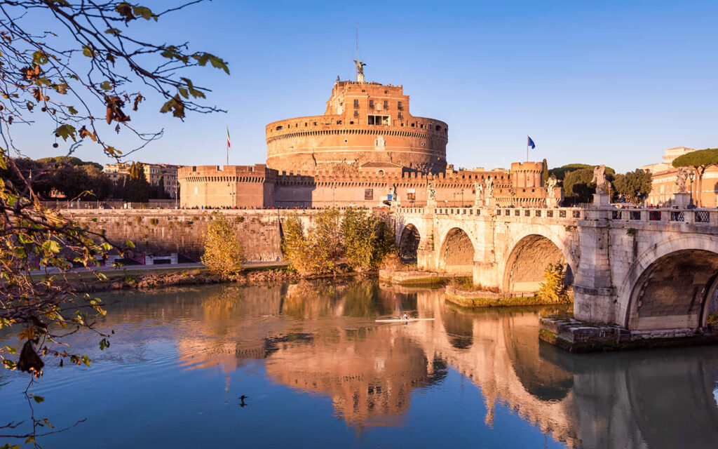 Castel Sant Angelo at sunset over Tiber River with stone bridge and lush greenery wallpaper background