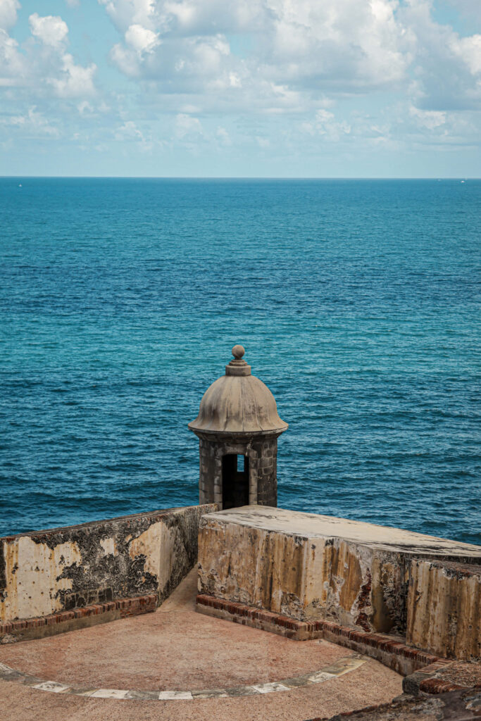 Stone sentry box on Castillo San Felipe del Morro overlooking ocean and cloudy sky background Wallpaper