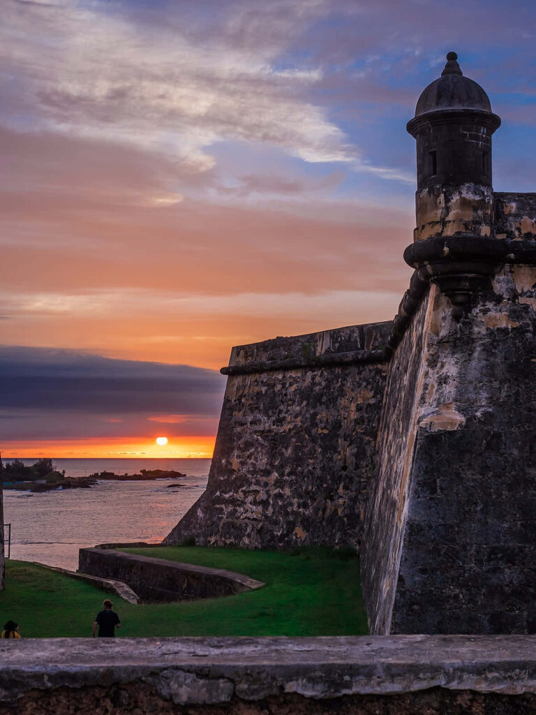 Sunset view of Castillo San Felipe del Morro fortress with ocean, green grass, and dramatic sky Wallpaper