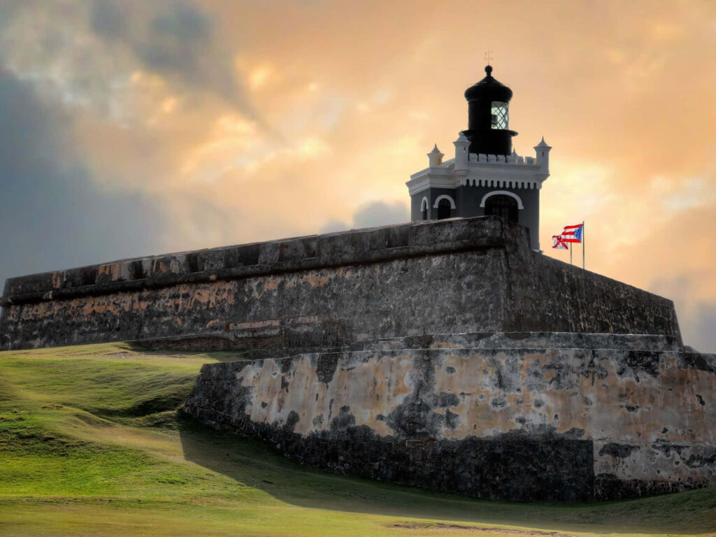 Castillo San Felipe del Morro lighthouse Puerto Rican flag green grass dramatic cloudy sky wallpaper