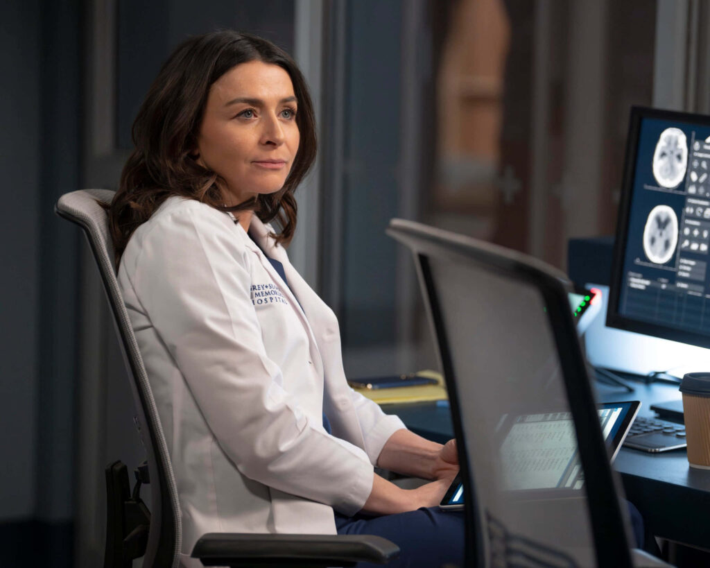 Caterina Scorsone in hospital lab coat seated at desk with medical monitors and coffee cup Wallpaper