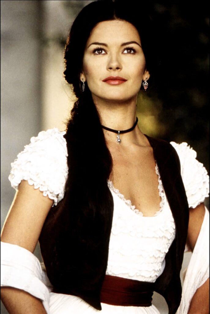 Catherine Zeta-Jones as Zorro in white ruffled dress brown vest elegant jewelry confident pose Wallpaper