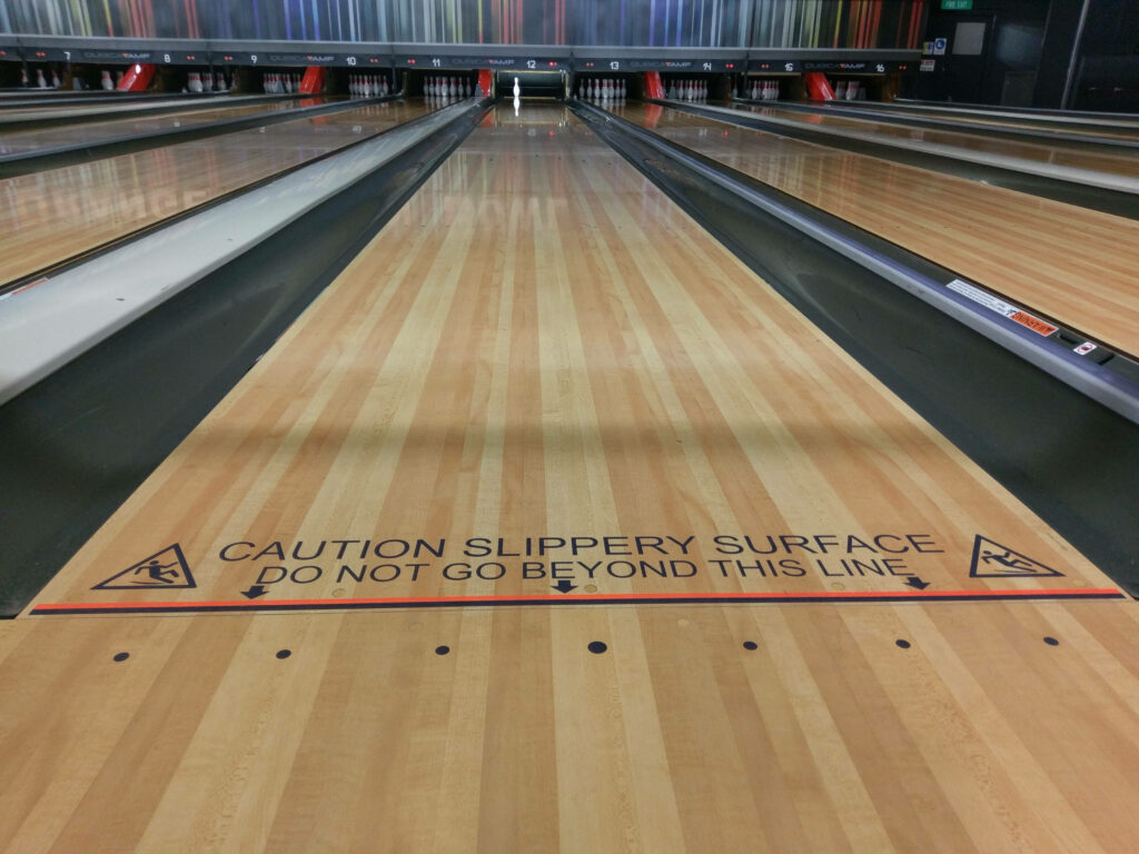 Caution sign on polished wooden bowling lane warning slippery surface modern bowling alley background Wallpaper