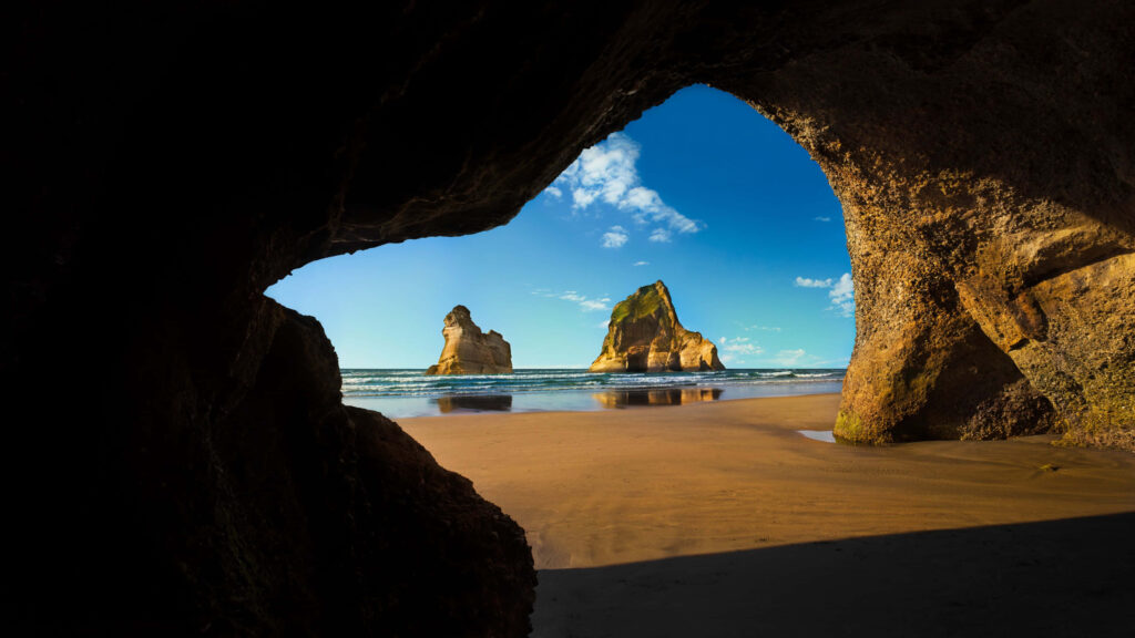 Cave View Wallpaper: Ocean Scene with Sunlit Shore and Rock Formations