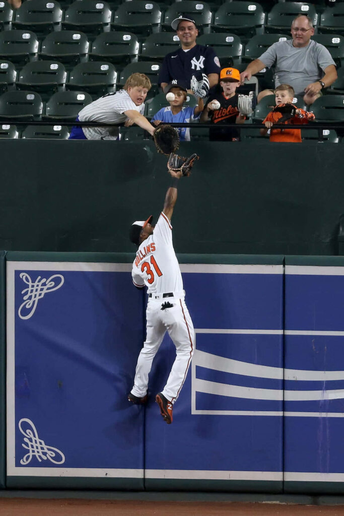 Cedric Mullins jumps at outfield wall making a spectacular MLB catch in orange white uniform Wallpaper