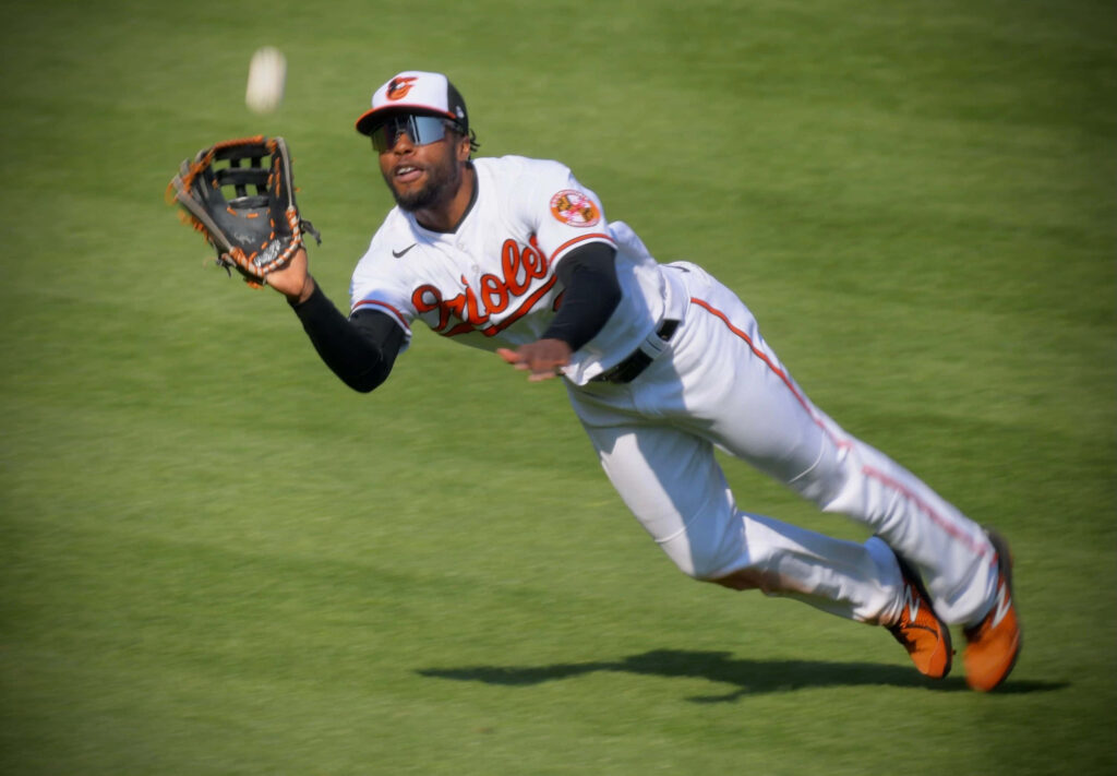 Cedric Mullins leaping for a dynamic catch in Orioles uniform on vibrant green baseball field Wallpaper