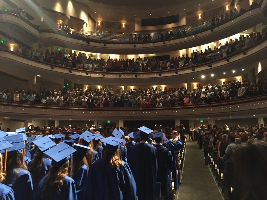 Graduates in blue caps and gowns at a grand multi tiered theater graduation ceremony wallpaper