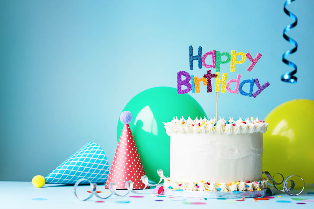Party-perfect: A vibrant birthday cake steals the show amidst a cheerful backdrop of balloons and party hat Wallpaper