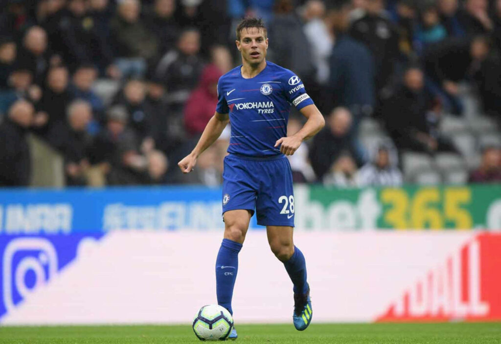 César Azpilicueta in blue Chelsea kit with captain armband leading on football pitch action shot Wallpaper