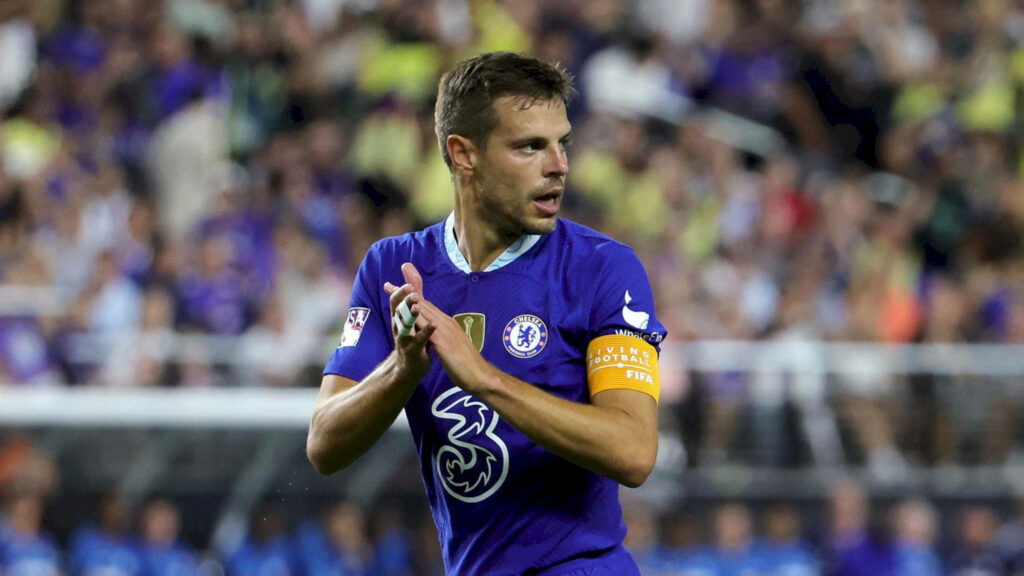César Azpilicueta in vibrant Chelsea kit showing determination on pitch with lively stadium crowd Wallpaper