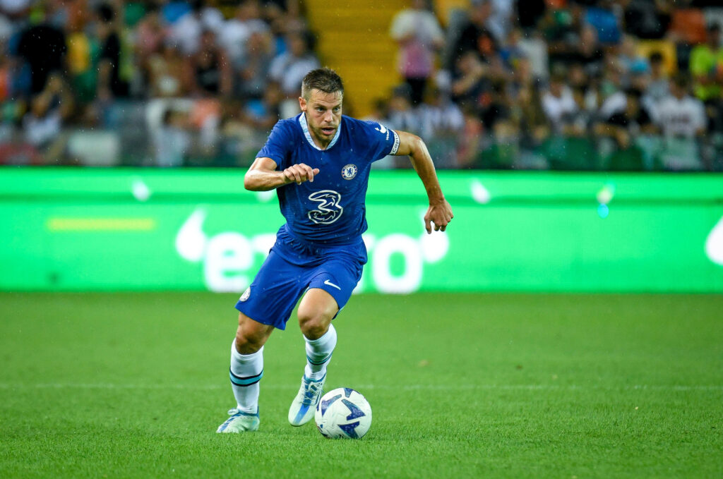 César Azpilicueta running in Chelsea blue kit on green pitch with blurred stadium crowd background Wallpaper