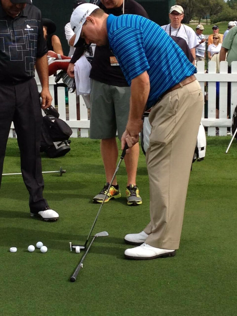 Chad Campbell focused putting in blue striped shirt on vibrant green golf course with golf balls Wallpaper