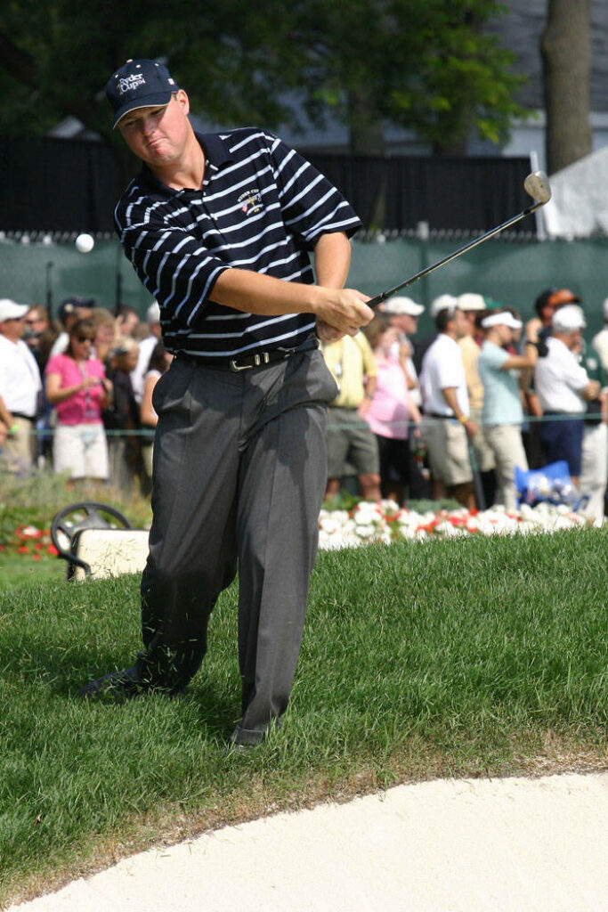 Chad Campbell mid golf swing on lush course near bunker wearing striped shirt and cap Wallpaper